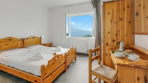 A wooden bed with a white mattress, a wooden desk with a chair, a window with a view of a mountain, and a ceiling fan.