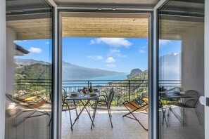 A balcony with a table set for dining, a chair, and a view of a mountainous landscape and lake.