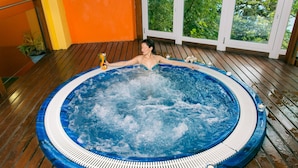 Iemand ontspant in een hottub met een houten terras en uitzicht op groen.