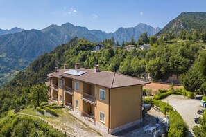 Un edificio de varios pisos con balcones, un camino pavimentado y vistas a montañas circundantes.
