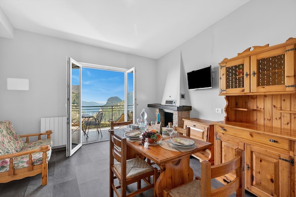 A dining area with a wooden table, chairs, and a view through an open door to a balcony.