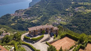A multi-story building with a tennis court, surrounded by lush greenery and a mountainous backdrop. - Residence Bellevue 3, Tremosine, Italy (Tremosine)