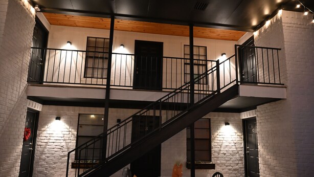 Un interior de varios niveles con una escalera, paredes de ladrillo blanco y barandillas negras.