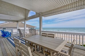 Ein überdachter Außenbereich mit Holztisch und -stühlen mit Blick auf den Strand.
