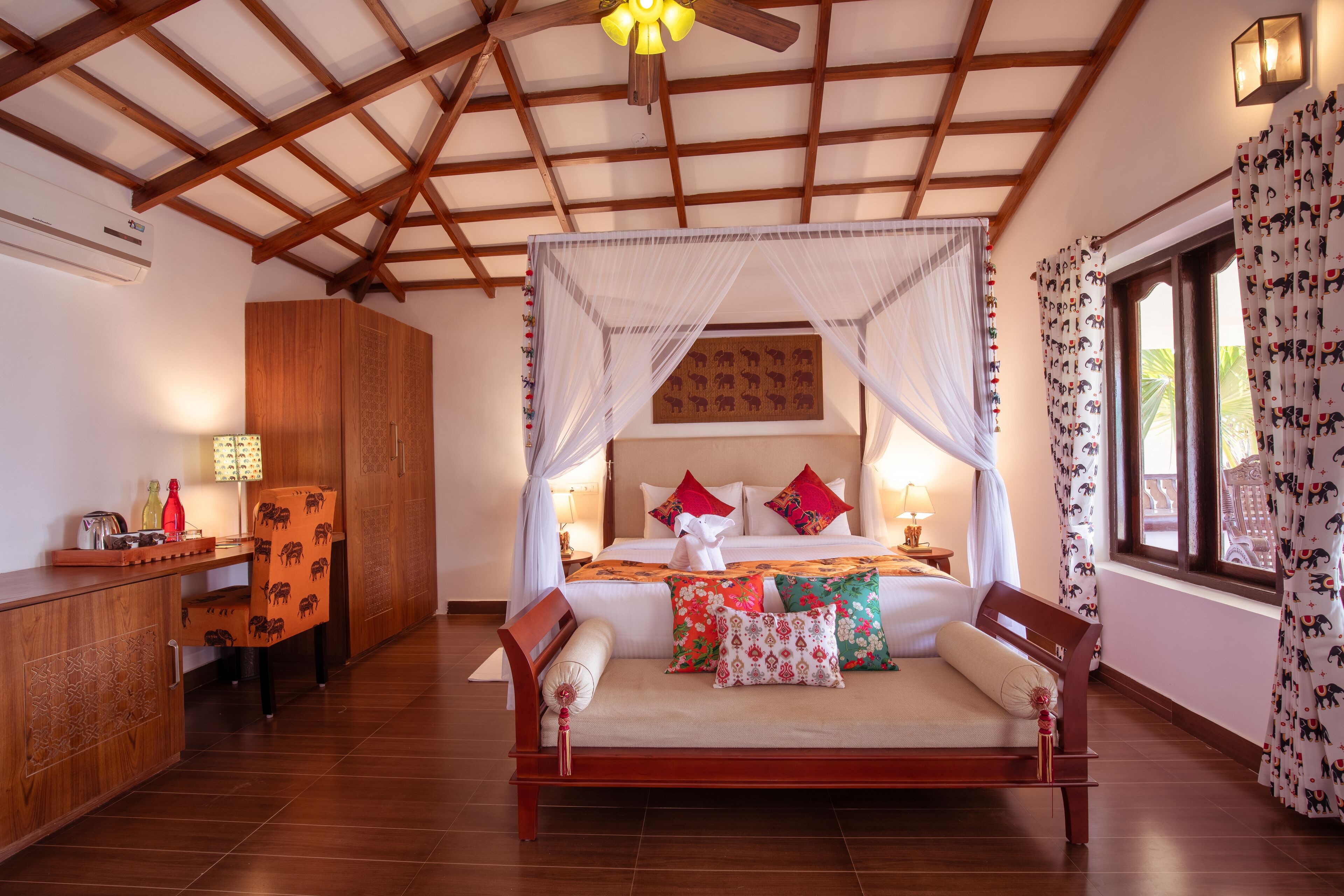 A spacious bedroom with a wooden bed, a nightstand, a desk, and a large window with curtains.
