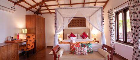A spacious bedroom with a wooden bed, a nightstand, a desk, and a large window with curtains.
