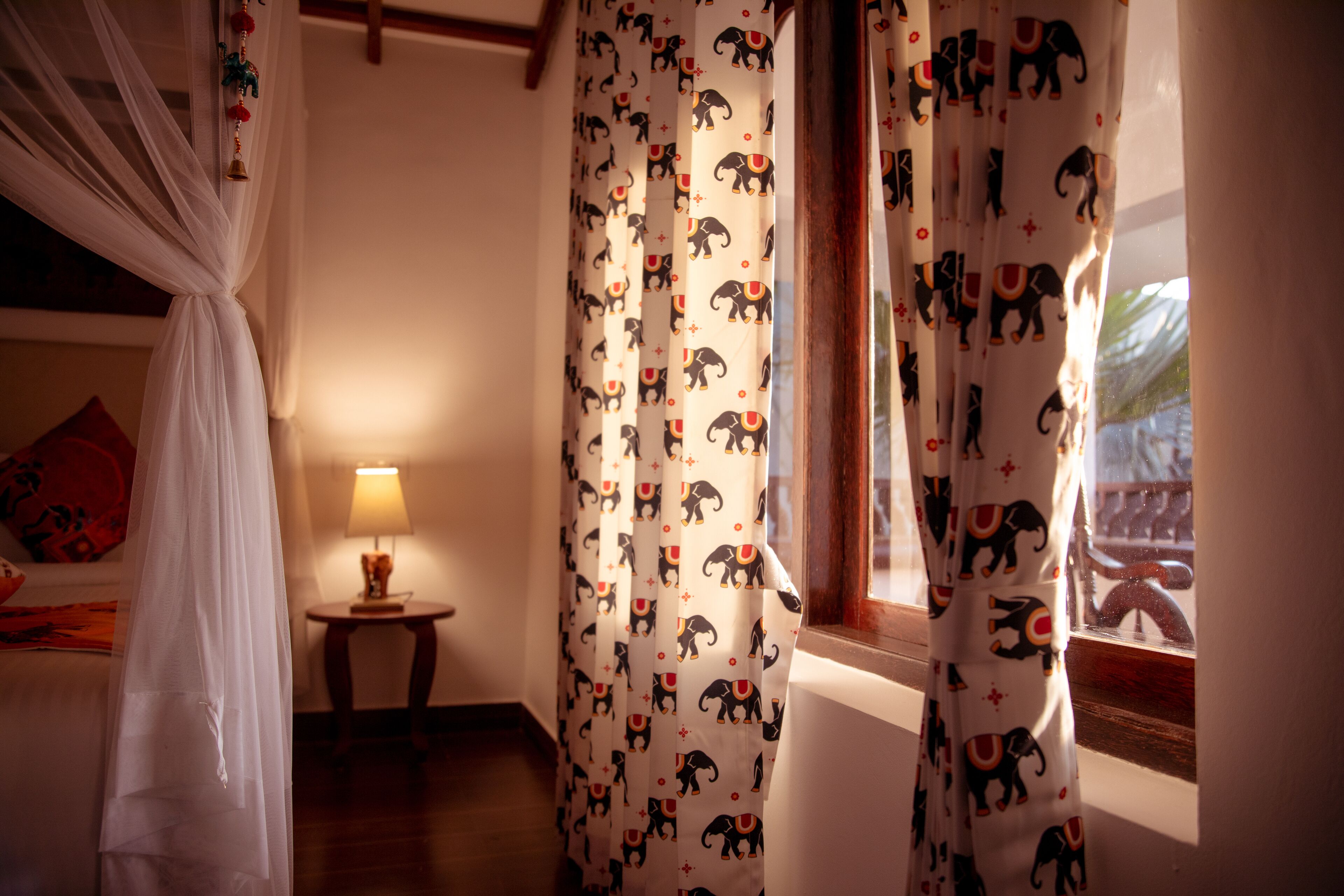 A bedroom with a bed, a bedside table with a lamp, and curtains with elephant patterns.