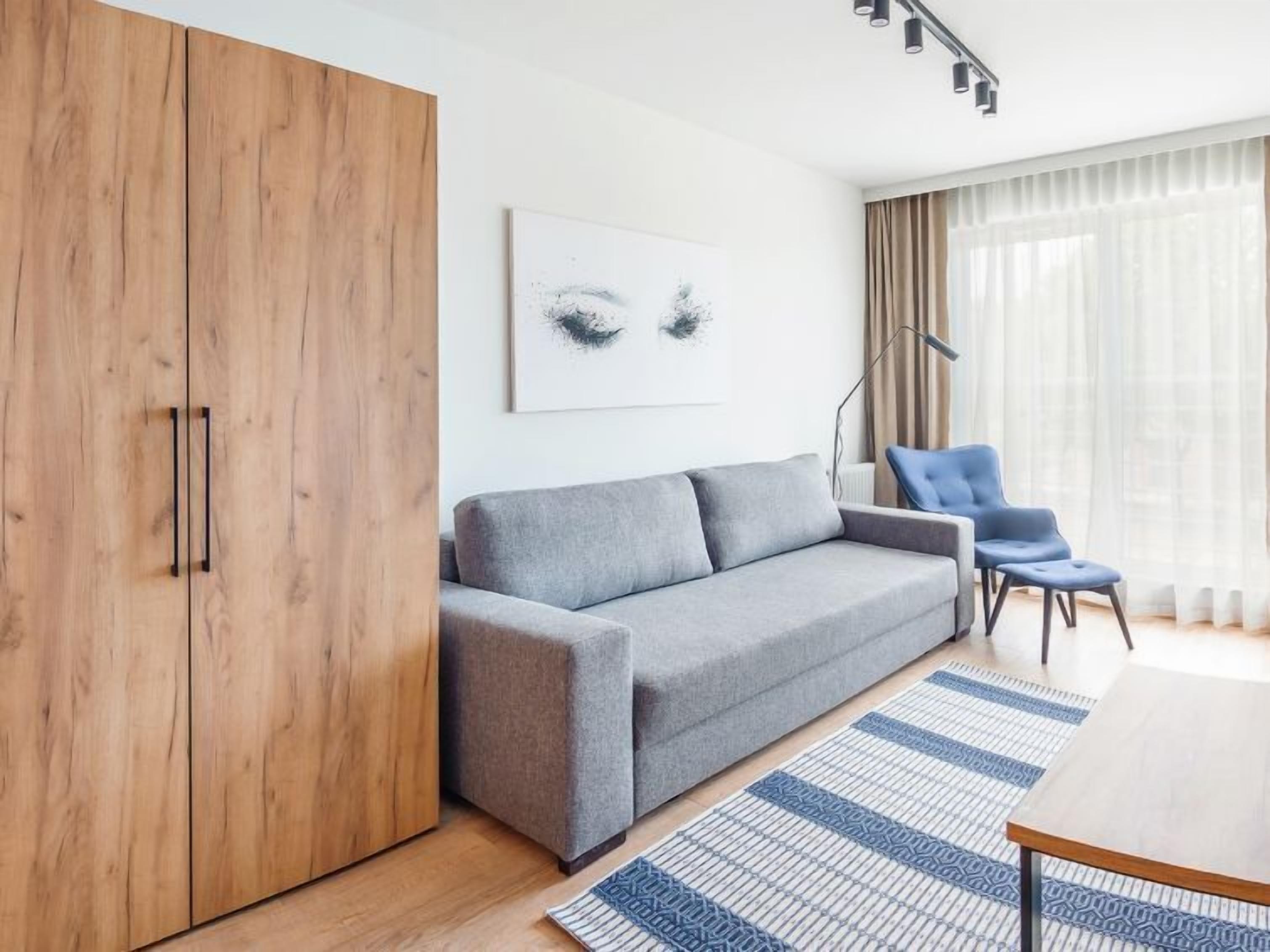 Ein modernes Wohnzimmer mit einem grauen Sofa, einem Holzschrank, einem blauen Sessel und einem Tisch.
