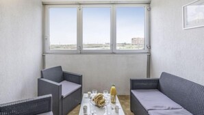 A small, modern room with two grey wicker sofas, a white coffee table, and a large window offering a view of a distant building and landscape. - Les terrasses de la Plage by Interhome (Cap d'Agde)