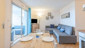 A modern living room with a sofa, a dining table set for two, and a television in the background. - Les terrasses de la Plage by Interhome (Cap d'Agde)