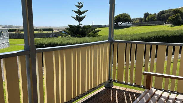 A wooden deck with a yellow railing, overlooking a well-maintained lawn and distant hills. - Sails - Elegant, spacious beach villa (Port Fairy)
