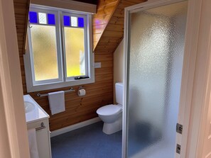 Un baño pequeño y funcional con inodoro, lavamanos y ventana con vidrios esmerilados.