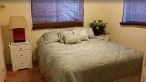 A bedroom with a bed, a nightstand, a lamp, and a potted plant.