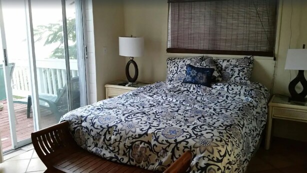 A bedroom with a bed, a chair, a nightstand, a lamp, and a window with blinds.