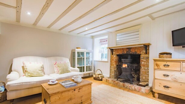A cozy living room with a white sofa, a wooden coffee table, a fireplace, and a television mounted on the wall. - Oast Barn Cottage by Bloom Stays -  2 guests  in 1 bedroom (Faversham)