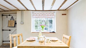 A dining area with a wooden table set for four, a window with floral curtains, and a sign on the wall. - Oast Barn Cottage by Bloom Stays -  2 guests  in 1 bedroom (Faversham)