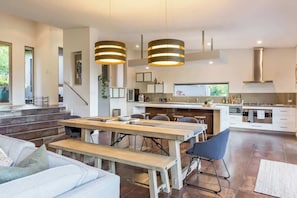 A modern kitchen with a dining area, wooden tables, and a staircase leading to an upper level. - Sunrise Tranquillity: Luxe Retreat with Heated Spa (Yallingup)