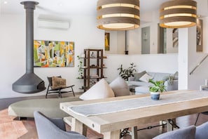A modern living room with a large painting, a fireplace, a dining table, and a staircase.