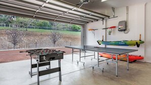 Et indendørs rekreativt område med et bordfodboldbord, et pingpongbord og kajakker.