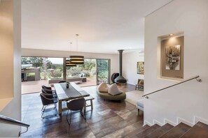 A modern interior with a dining area, a staircase, and a large window overlooking a garden.