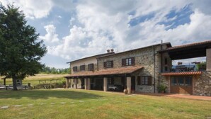 A stone house with a covered patio and a grassy yard.
