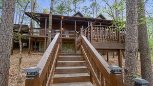 A wooden staircase leading to a cabin with a balcony, surrounded by trees.