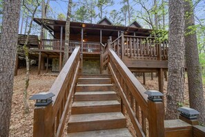 A wooden staircase leading to a cabin with a balcony, surrounded by trees.