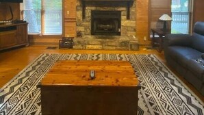 A spacious living room with a stone fireplace, wooden beams, and a large window.