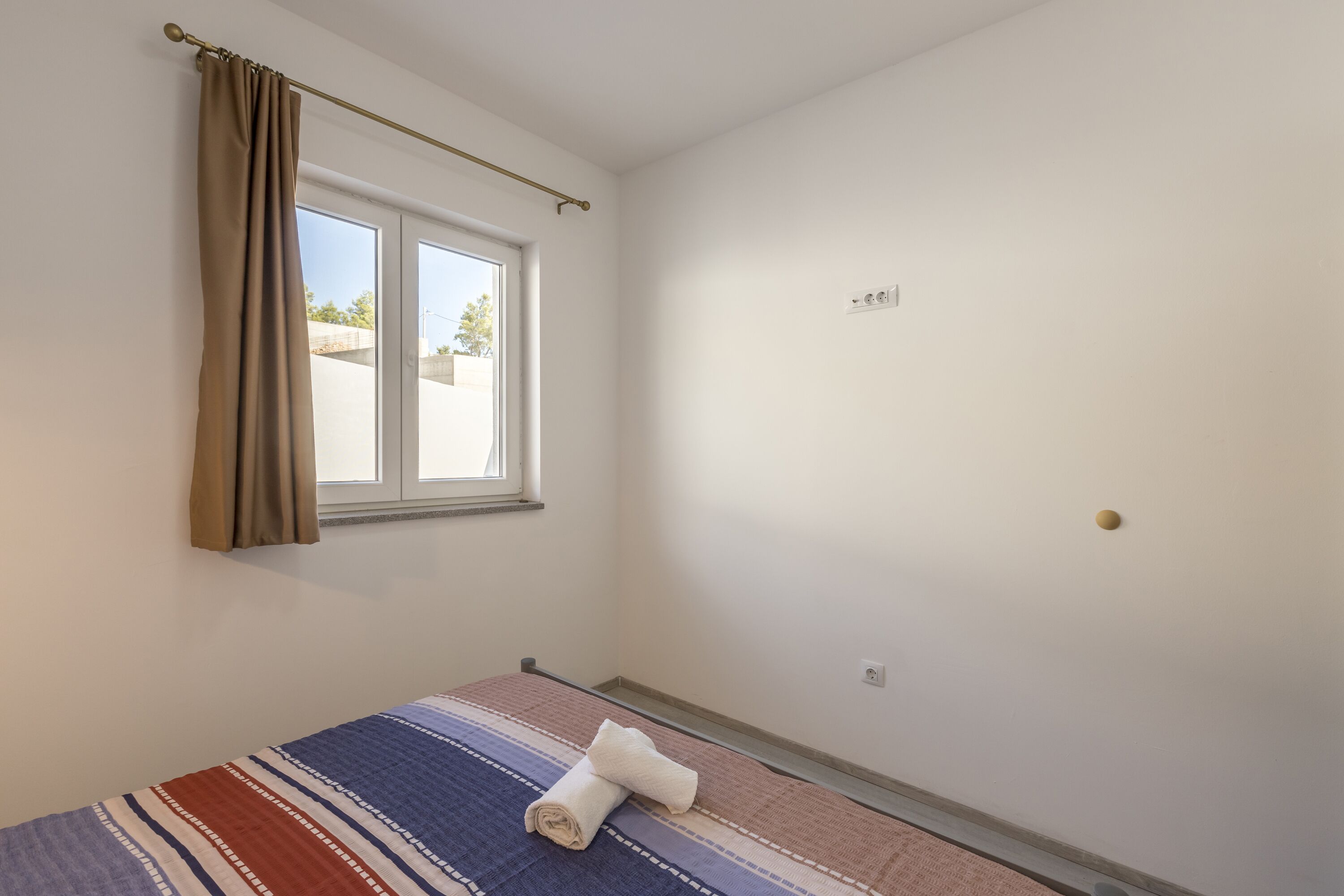 A small, clean room with a single bed, a window with curtains, and a plain wall.