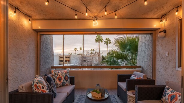A cozy outdoor seating area with wicker furniture, a large window overlooking palm trees and a cityscape. - BRAND NEW FULL LUXURY REMODEL - Old Town Scottsdale! 2BR/2BA En-suite, Htd Pool! (Scottsdale)
