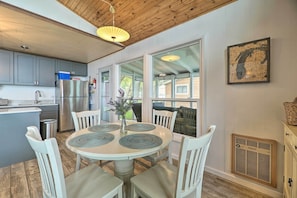 A modern kitchen with grey cabinets, a stainless steel refrigerator, and a dining area with a round table and white chairs.