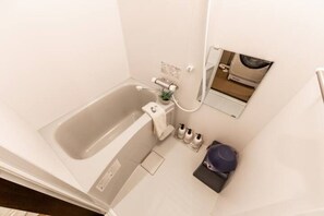 A small bathroom with a bathtub, a mirror, a towel rack, and a waste bin.