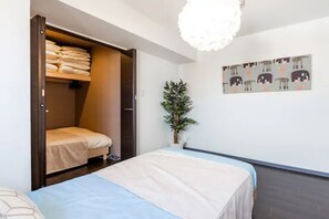 A bedroom with a bed, a wardrobe, a potted plant, and a wall with a pattern.