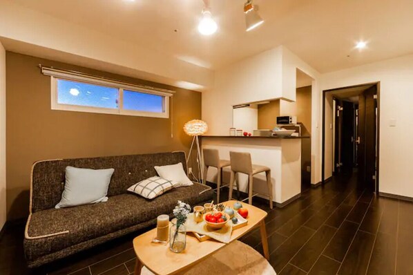 A modern living room with a sofa, a dining table with breakfast items, a kitchen area, and a view of the sky through a window.