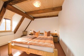 Una camera da letto con un letto di legno, due comodini con lampade, una finestra vista e un soffitto spiovente con travi a vista.