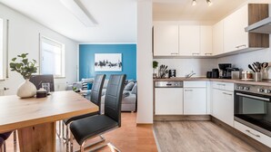 Eine moderne Küche mit weißen Schränken, einem eingebauten Ofen und einem Essbereich mit Holztisch und -stühlen.