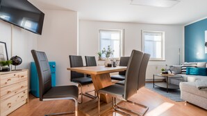 Ein modernes Wohnzimmer mit einem Holzesstisch, schwarzen Stühlen, einem grauen Sofa und einem flachbildfernseher an der Wand.