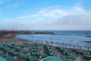 A beachside hotel with rows of green lounge chairs and umbrellas, a pier with a lifebuoy, and the ocean in the background. - Ca Veggia for Nature Lovers With Views & Garden (Stellanello)