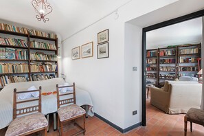 Een ruime woonkamer met een grote boekenkast, een comfortabele bank en een eethoek met stoelen.