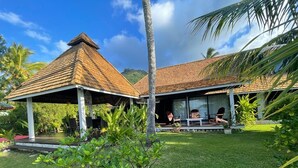 A bungalow with a tiled roof, a covered patio, and a lush garden. - Pension Poerani Moorea - DeLuxe Suite, living room, kitchen, 2 bedrooms a/c (Moorea)