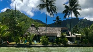 A beachfront property with a thatched-roof building, clear turquoise water, and palm trees. - Pension Poerani Moorea - DeLuxe Suite, living room, kitchen, 2 bedrooms a/c (Moorea)