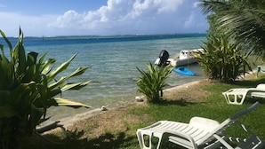 A beach scene with a boat, lounge chairs, and tropical plants. - Pension Poerani Moorea - DeLuxe Suite, living room, kitchen, 2 bedrooms a/c (Moorea)