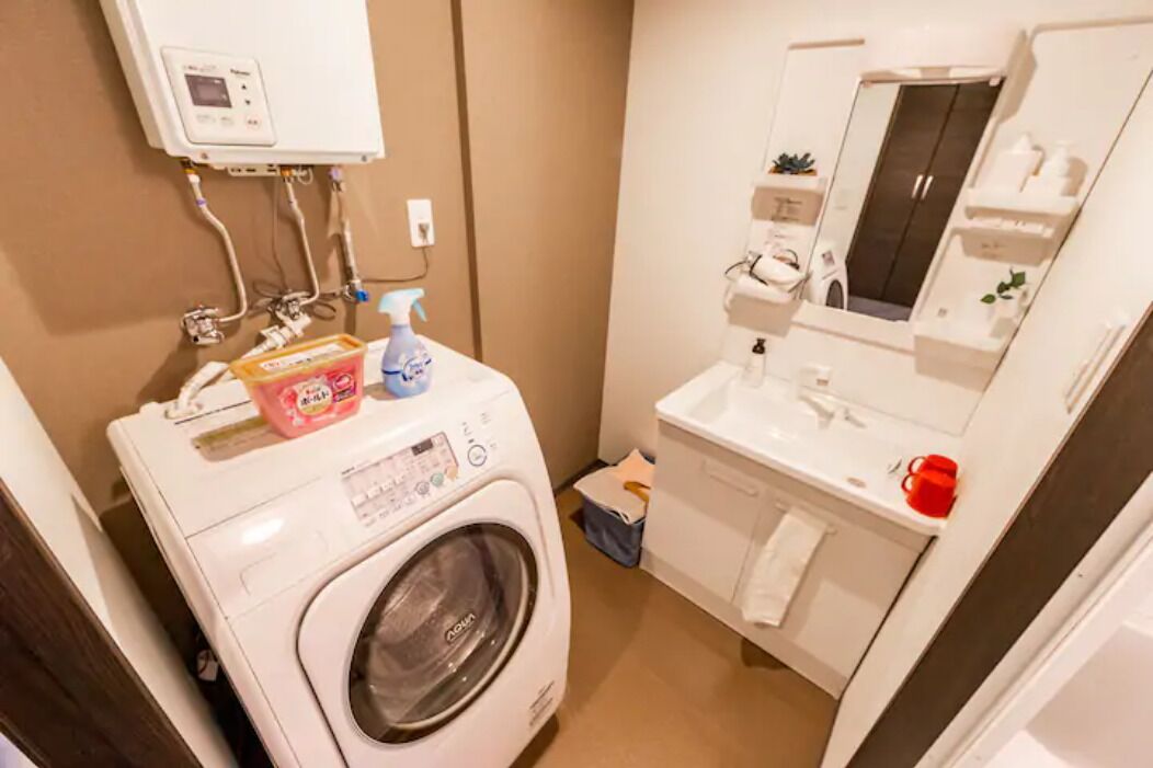 A compact bathroom with a washing machine, a sink, and a mirror.