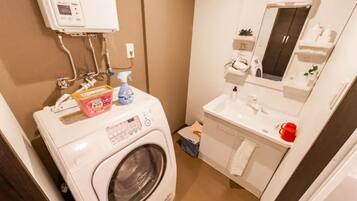 A compact bathroom with a washing machine, a sink, and a mirror.