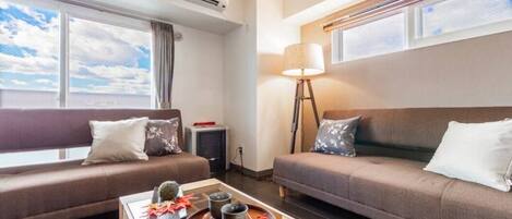 A modern hotel room with two sofas, a coffee table with a tray, and a standing lamp.