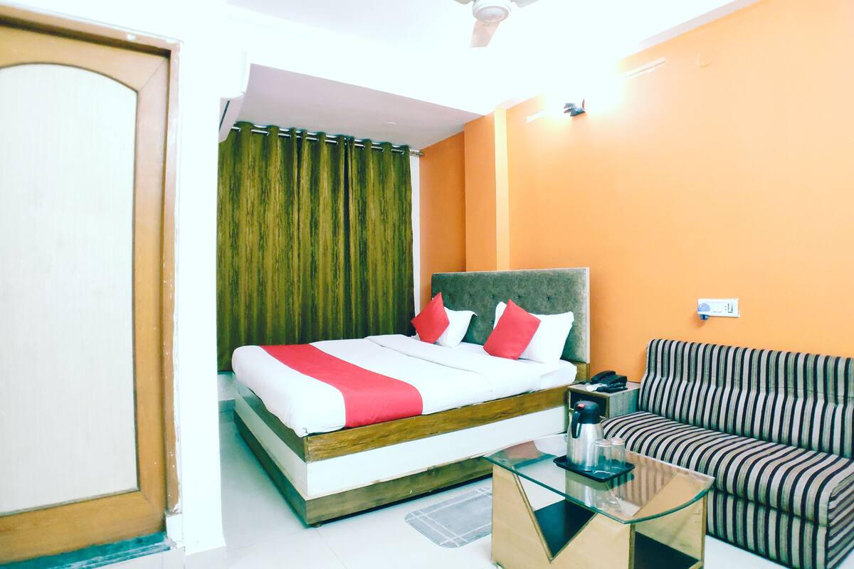 A hotel room with a bed, a sofa, a glass coffee table, a ceiling fan, and a window with curtains.
