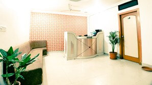 A reception desk with a globe and a sign, a ceiling fan, a reception area, a door, and a potted plant. - Hotel 4 Seasons (Bhopal)