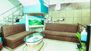 A living room with a glass coffee table, two brown sofas, a fish tank, and a ceiling fan. - Hotel 4 Seasons (Bhopal)