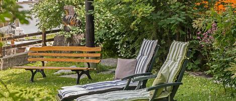A garden with a wooden bench and two lounge chairs.