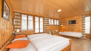 Habitación con paneles de madera, dos camas, una silla, un televisor y una ventana con cortinas.